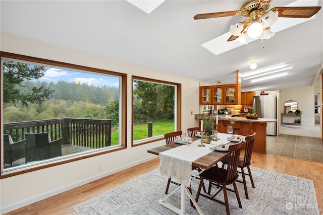 dining area featuring lofted ceiling with skylight, light wood-type flooring, and ceiling fan