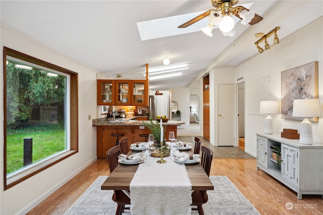 dining area with vaulted ceiling with skylight, light hardwood / wood-style floors, and ceiling fan