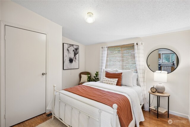 bedroom with a textured ceiling, vaulted ceiling, and hardwood / wood-style flooring