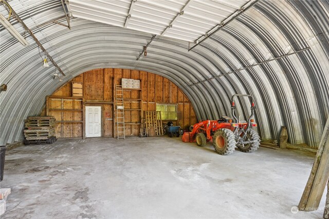 miscellaneous room with vaulted ceiling, concrete flooring, and wood walls