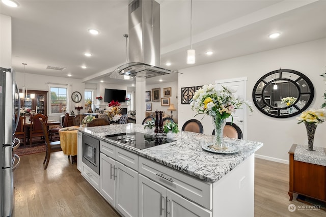 kitchen featuring island range hood, white cabinetry, appliances with stainless steel finishes, decorative light fixtures, and light hardwood / wood-style flooring