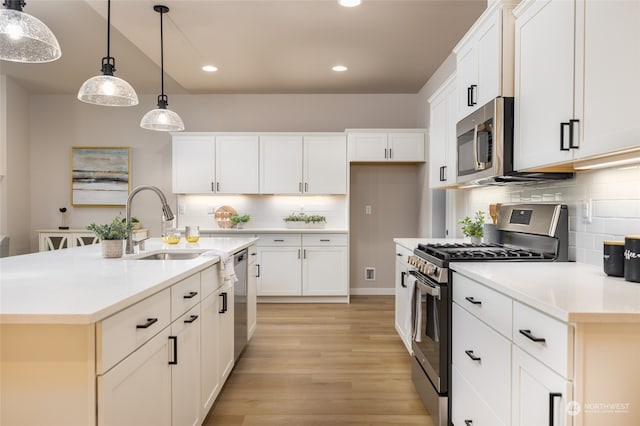 kitchen with tasteful backsplash, stainless steel appliances, decorative light fixtures, a center island with sink, and white cabinetry