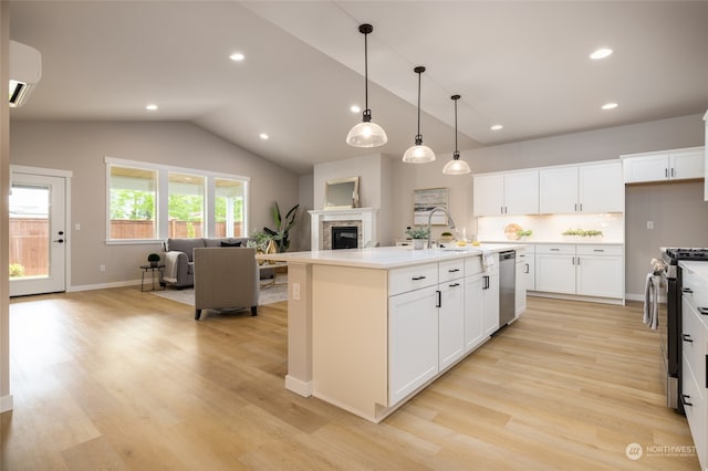 kitchen with stainless steel appliances, decorative light fixtures, an AC wall unit, white cabinets, and an island with sink