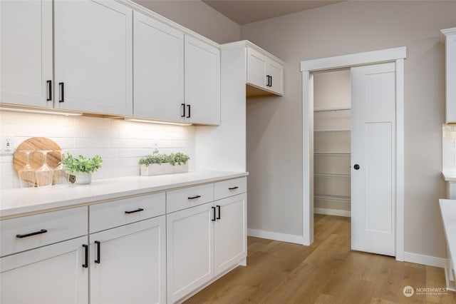 interior space featuring backsplash, white cabinets, and light wood-type flooring