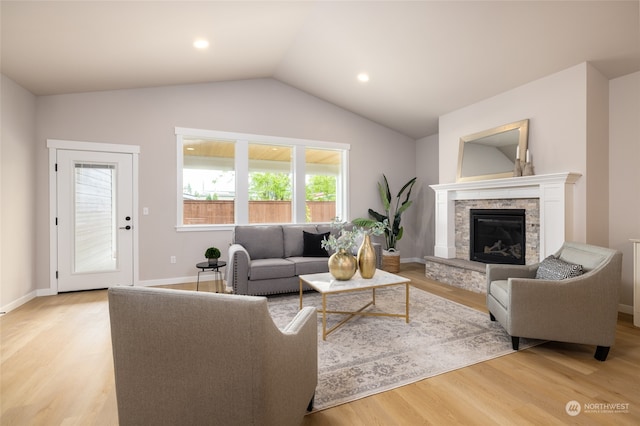 living room with a stone fireplace, a wealth of natural light, lofted ceiling, and light wood-type flooring