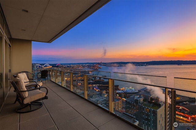 balcony at dusk featuring a water view