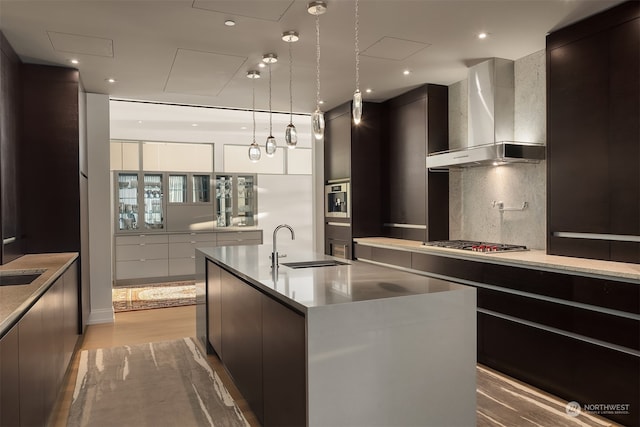 kitchen with sink, wall chimney exhaust hood, a spacious island, light hardwood / wood-style floors, and decorative backsplash