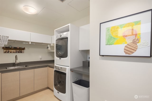 washroom featuring sink, stacked washing maching and dryer, and cabinets