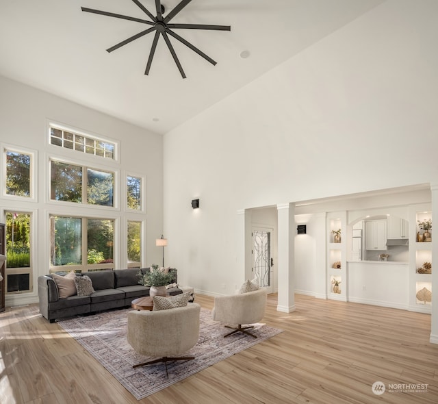 living room featuring decorative columns, high vaulted ceiling, ceiling fan, and light hardwood / wood-style flooring