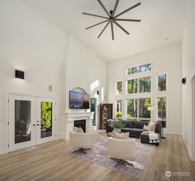 living room featuring french doors, a high ceiling, light wood-type flooring, and ceiling fan