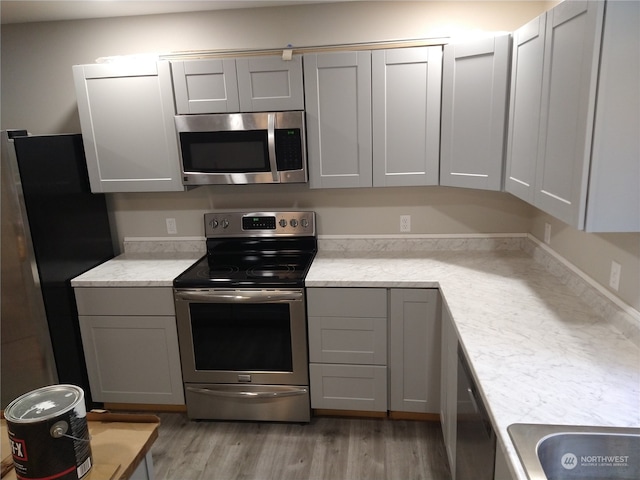 kitchen with appliances with stainless steel finishes, gray cabinets, and light hardwood / wood-style floors