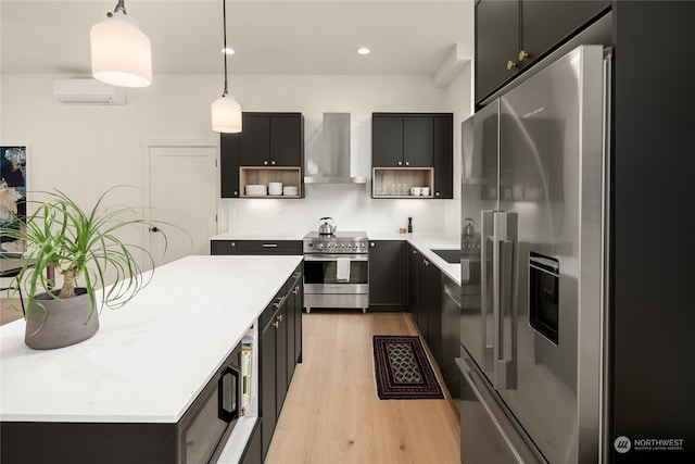 kitchen with wall chimney range hood, pendant lighting, light hardwood / wood-style flooring, a wall mounted AC, and appliances with stainless steel finishes