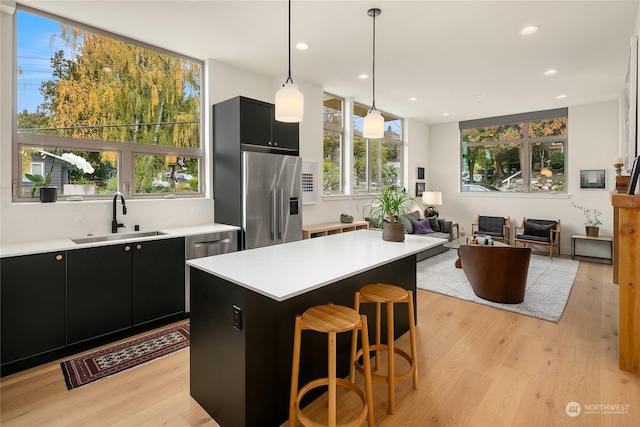 kitchen featuring light wood-type flooring, decorative light fixtures, sink, stainless steel appliances, and a center island