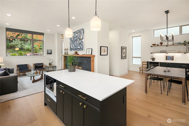 kitchen with an inviting chandelier, pendant lighting, a kitchen island, light hardwood / wood-style flooring, and built in microwave