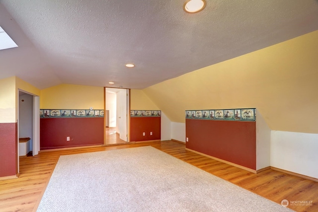 additional living space featuring wood-type flooring, a textured ceiling, and vaulted ceiling with skylight