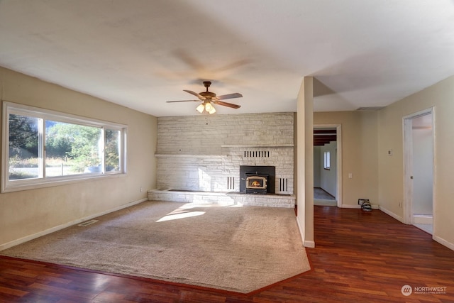 unfurnished living room featuring a wood stove, ceiling fan, and dark hardwood / wood-style flooring