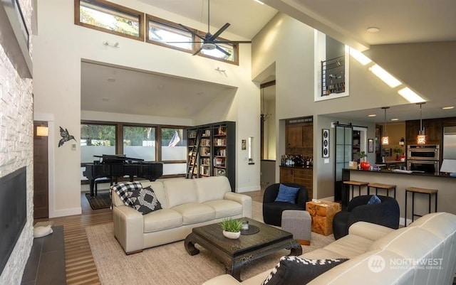 living room featuring light hardwood / wood-style flooring, high vaulted ceiling, ceiling fan, and a stone fireplace