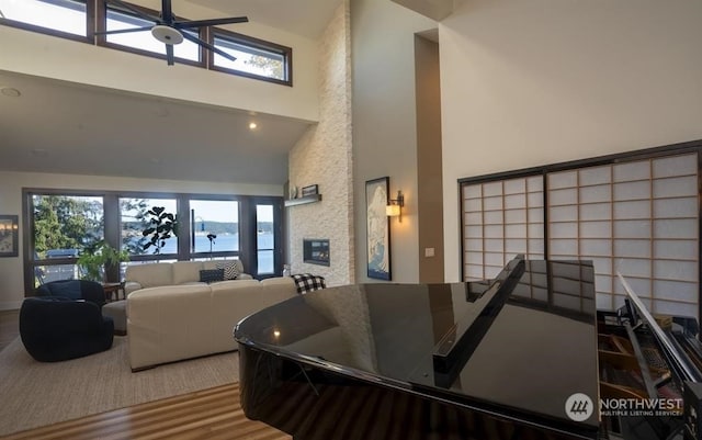 interior space with ceiling fan, a water view, a stone fireplace, and high vaulted ceiling