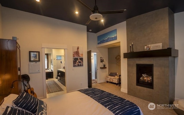 bedroom with a tiled fireplace, connected bathroom, light colored carpet, and ceiling fan