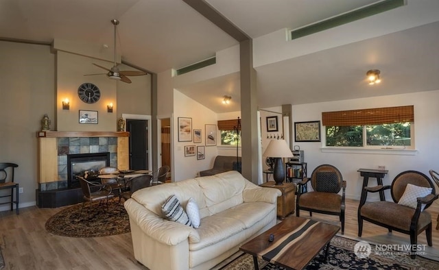 living room featuring ceiling fan, lofted ceiling, a tiled fireplace, and light wood-type flooring