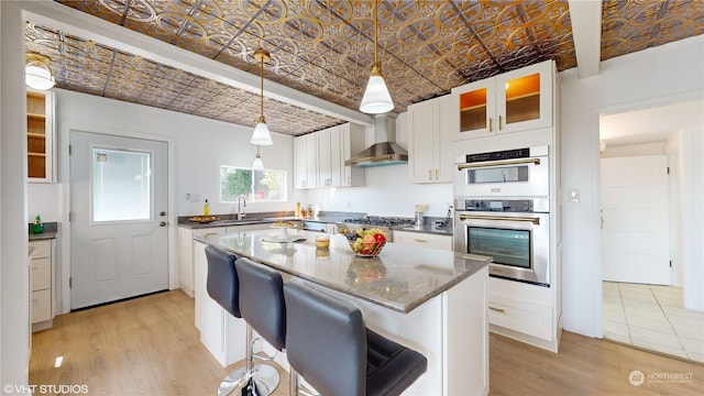 kitchen featuring a kitchen island, light wood-type flooring, stainless steel appliances, wall chimney exhaust hood, and white cabinetry