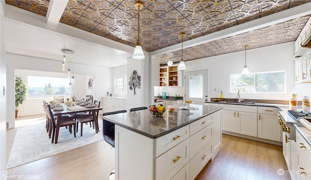 kitchen with white cabinets, hanging light fixtures, sink, a center island, and light wood-type flooring