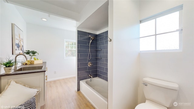 full bathroom featuring wood-type flooring, vanity, tiled shower / bath combo, and toilet