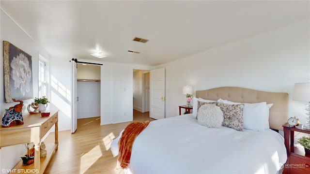 bedroom with a barn door, a closet, a walk in closet, and light wood-type flooring