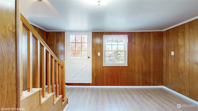 foyer entrance featuring crown molding, wood walls, and light hardwood / wood-style floors