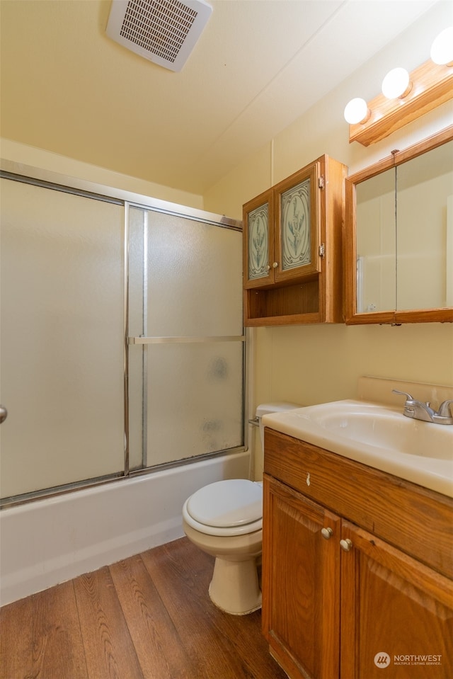 full bathroom featuring bath / shower combo with glass door, hardwood / wood-style floors, vanity, and toilet