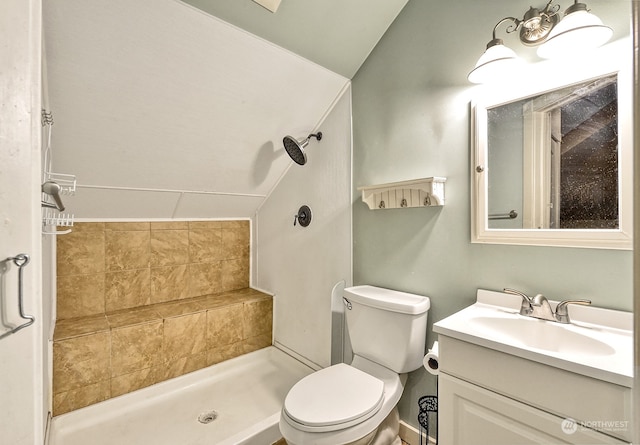 bathroom with vanity, lofted ceiling, tiled shower, and toilet