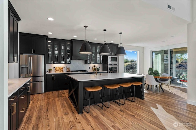 kitchen featuring tasteful backsplash, stainless steel appliances, light wood-type flooring, and an island with sink