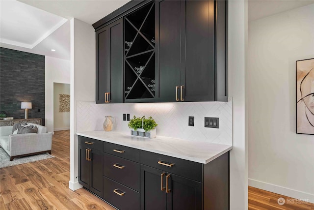 bar with tasteful backsplash, light stone countertops, and light hardwood / wood-style flooring