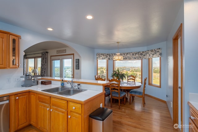 kitchen featuring sink, light wood-type flooring, dishwasher, kitchen peninsula, and decorative light fixtures