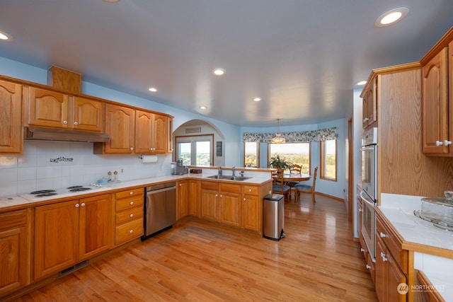 kitchen featuring appliances with stainless steel finishes, light hardwood / wood-style flooring, pendant lighting, tile counters, and sink