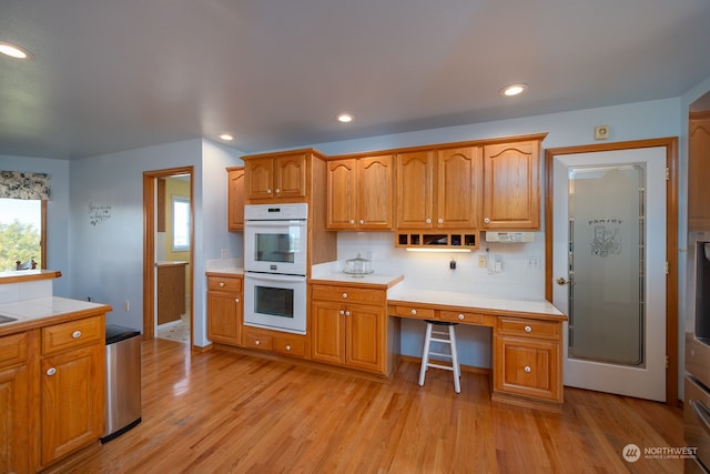 kitchen with built in desk, tasteful backsplash, white double oven, and light wood-type flooring