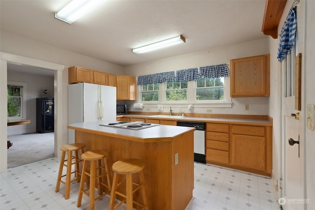 kitchen featuring a kitchen bar, white appliances, plenty of natural light, and a kitchen island