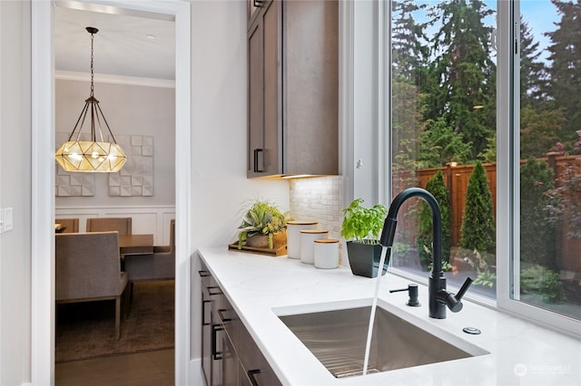 kitchen featuring light stone countertops, dark brown cabinetry, decorative backsplash, sink, and decorative light fixtures