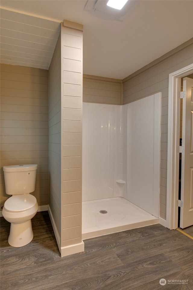 bathroom with hardwood / wood-style flooring, wooden walls, walk in shower, and toilet