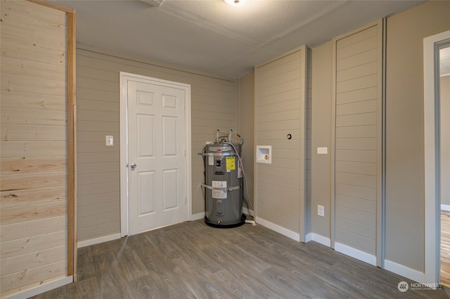 basement with wooden walls, water heater, dark hardwood / wood-style flooring, and a textured ceiling