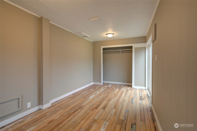 unfurnished bedroom featuring wood walls, a closet, light hardwood / wood-style flooring, and ornamental molding