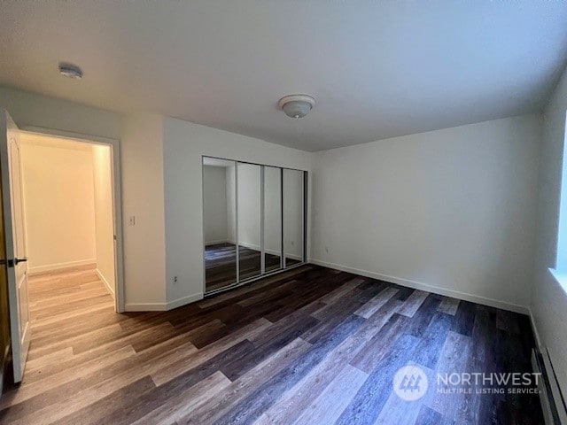 unfurnished bedroom with hardwood / wood-style floors, a baseboard heating unit, and a closet