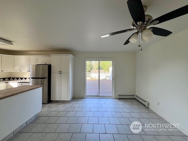 kitchen featuring a baseboard heating unit, white cabinetry, ceiling fan, stainless steel refrigerator, and light tile patterned floors