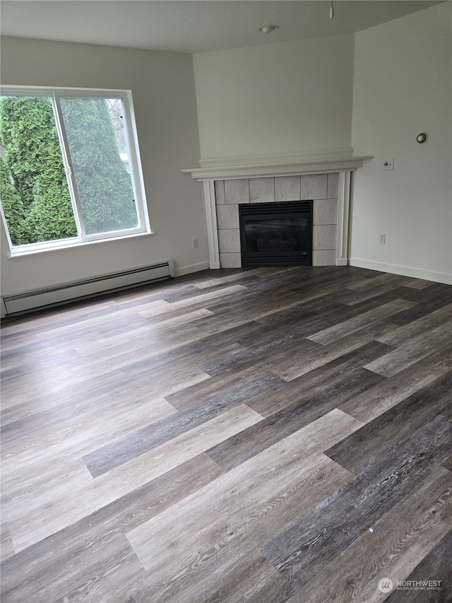 unfurnished living room featuring baseboard heating, vaulted ceiling, hardwood / wood-style flooring, and a tile fireplace