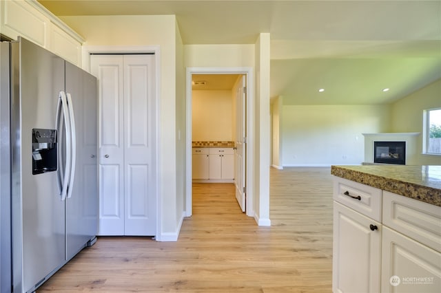 kitchen with stainless steel fridge with ice dispenser, light wood-type flooring, white cabinetry, and dark stone counters