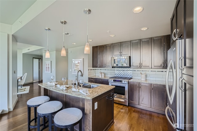 kitchen with light stone countertops, sink, an island with sink, stainless steel appliances, and pendant lighting