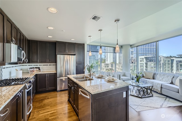 kitchen with a kitchen island with sink, backsplash, hardwood / wood-style floors, sink, and appliances with stainless steel finishes