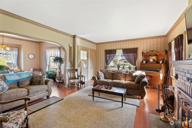 living room with ornamental molding, an inviting chandelier, hardwood / wood-style floors, and a fireplace