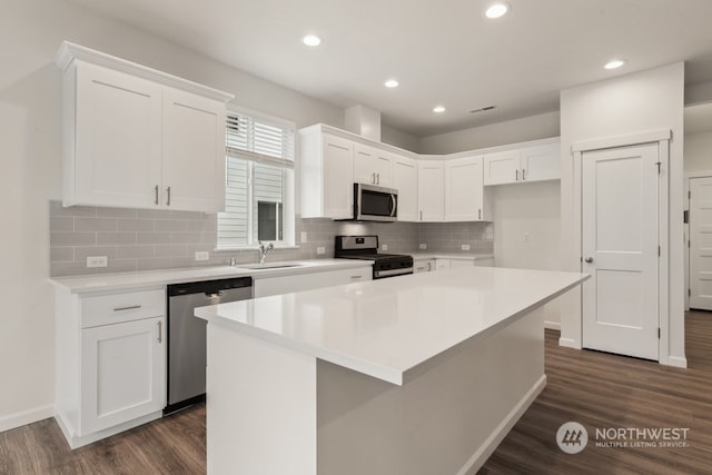 kitchen with sink, a kitchen island, white cabinetry, stainless steel appliances, and dark hardwood / wood-style floors