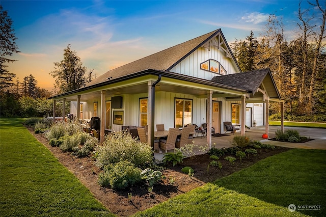 back of property at dusk featuring an attached garage, a yard, board and batten siding, an outdoor hangout area, and a shingled roof